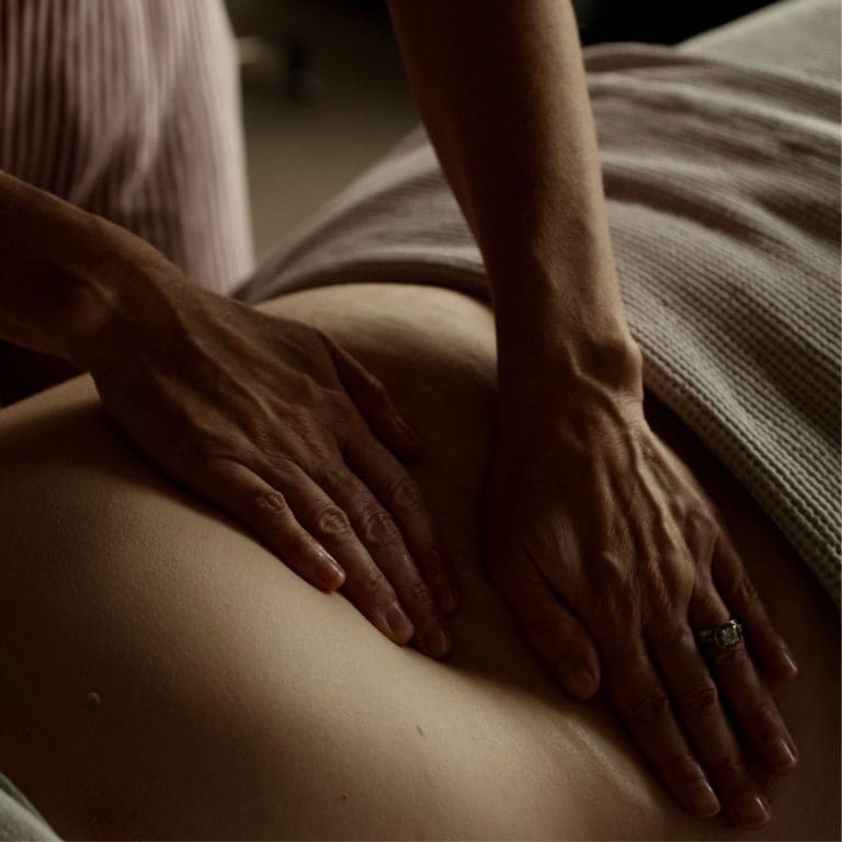 Hands performing therapeutic bodywork on a woman’s lower abdomen